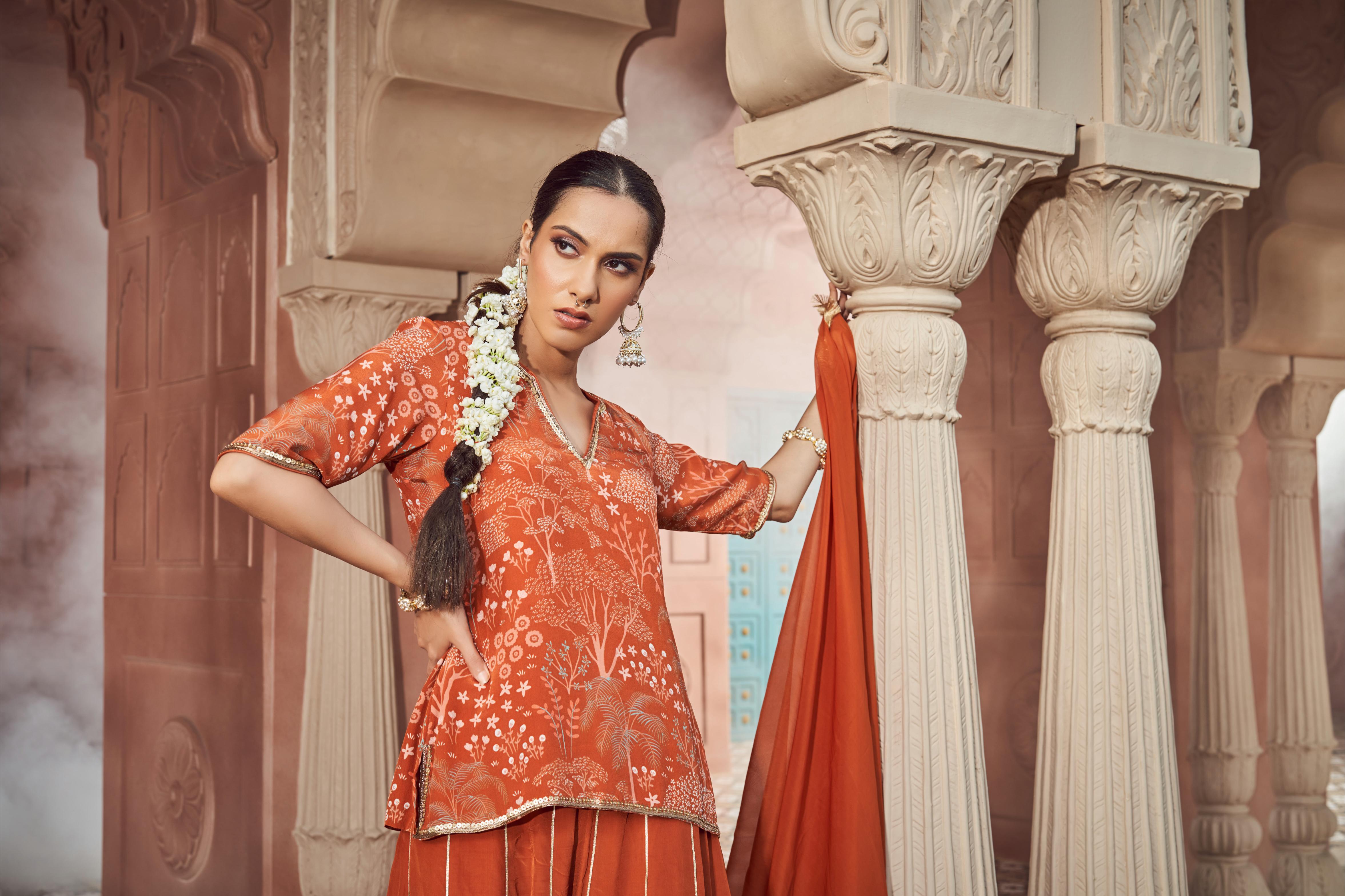 Featuring rust orange printed and embroidered short kurti paired with crepe sharara and organza dupatta