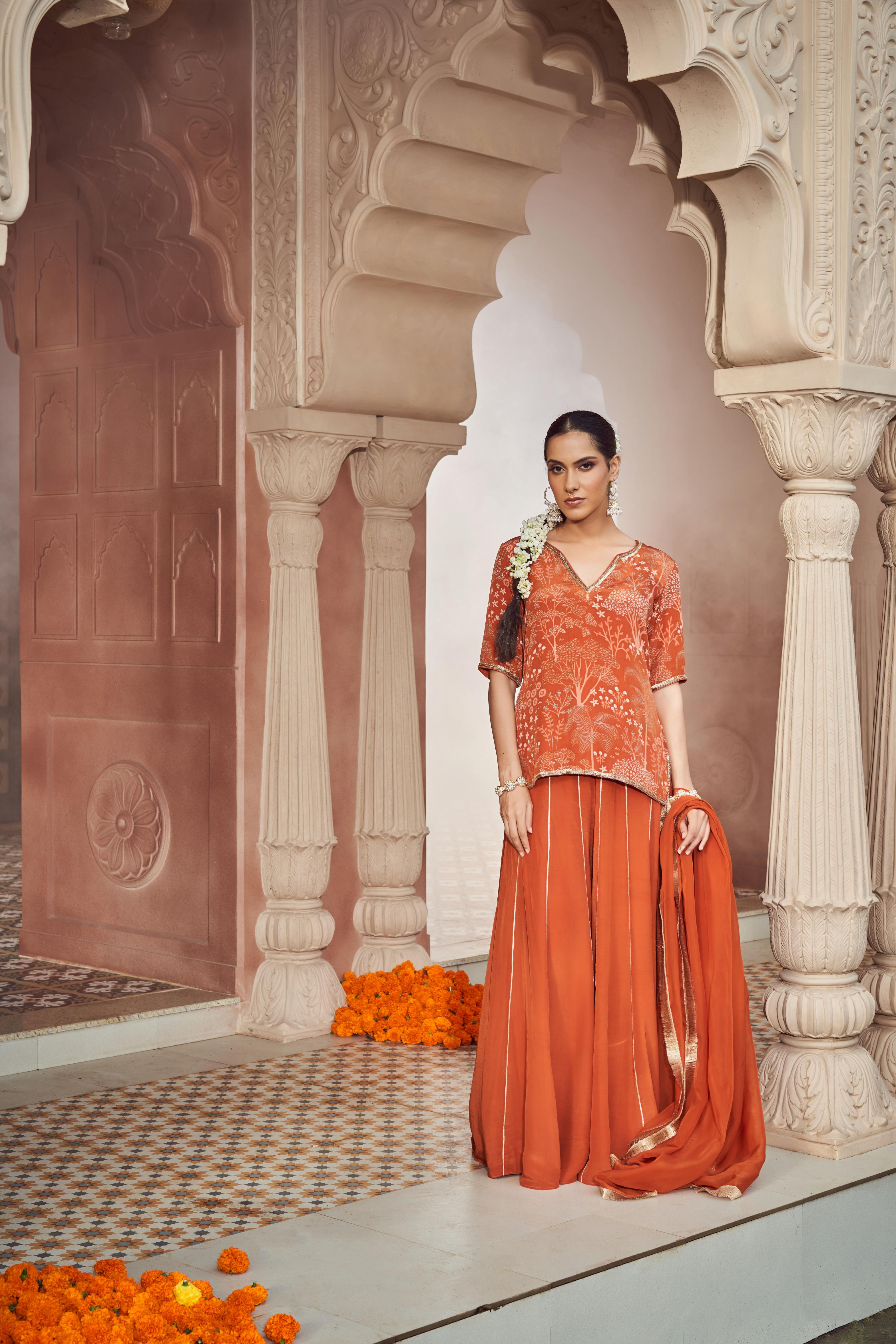 Featuring rust orange printed and embroidered short kurti paired with crepe sharara and organza dupatta